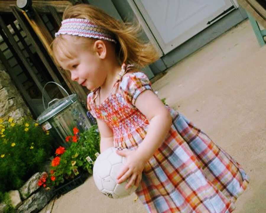 Emily in colorful headband and dress holding a miniature soccer ball.