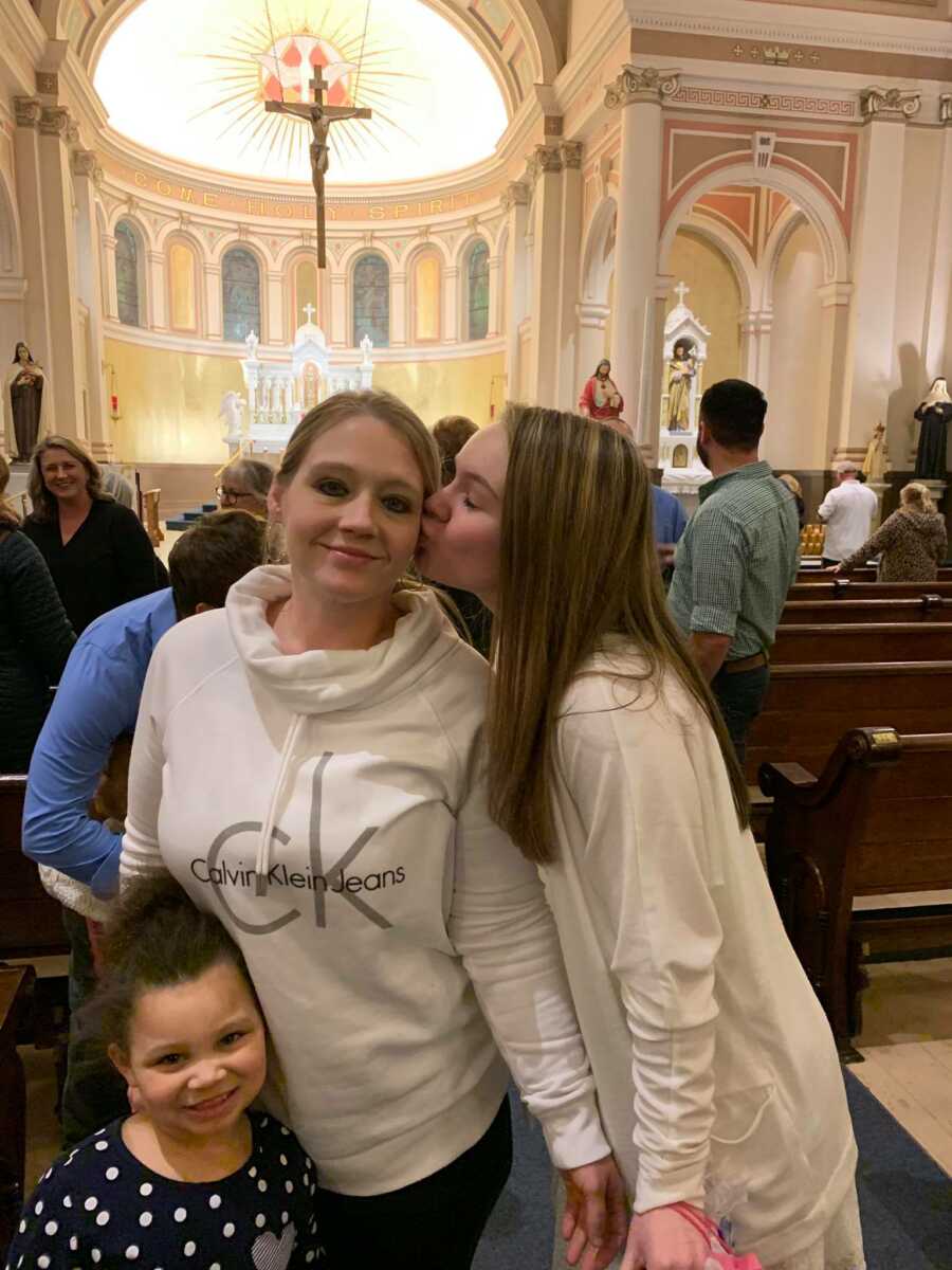 Daughter kissing her mother on the cheek in a church.