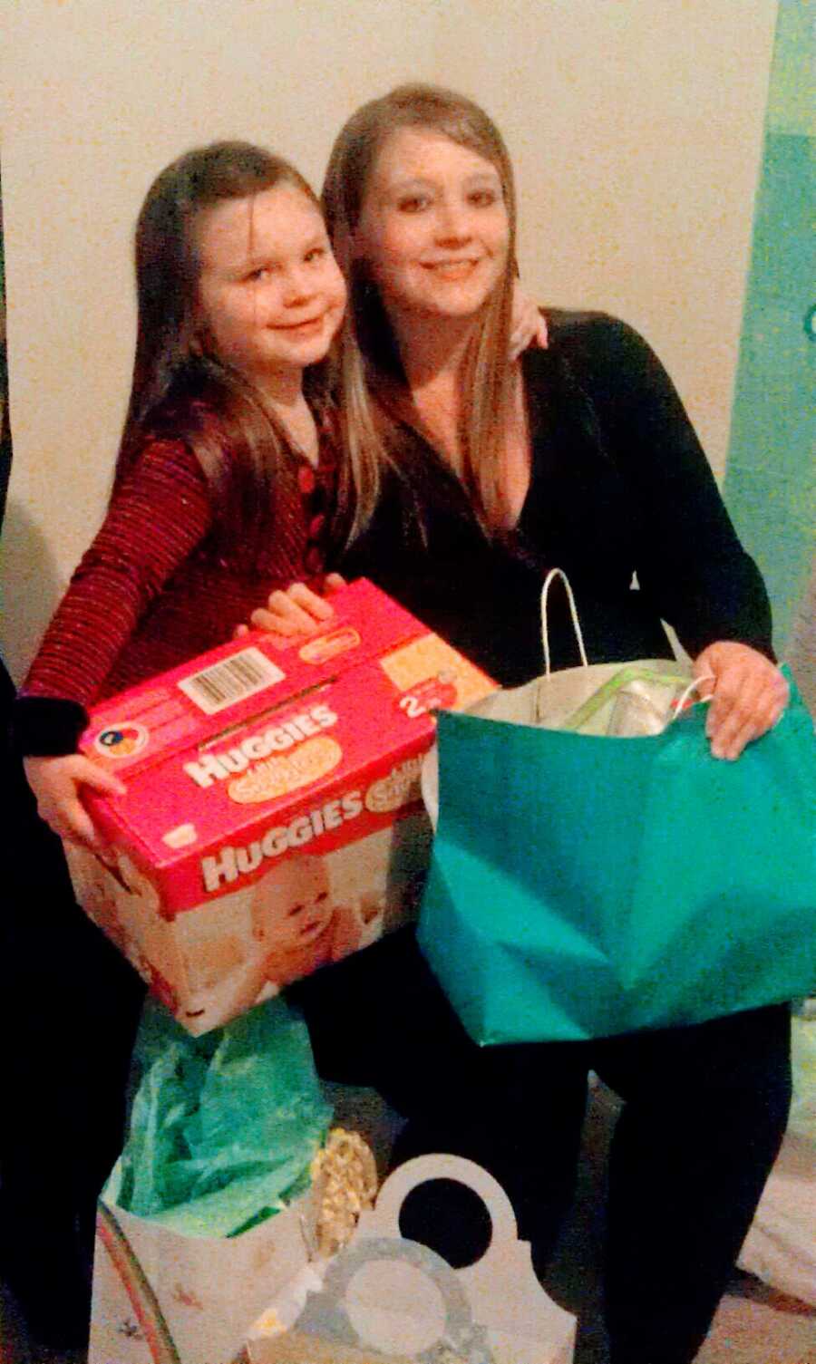 Mom and daughter holding Huggies diapers and a bag of other items.