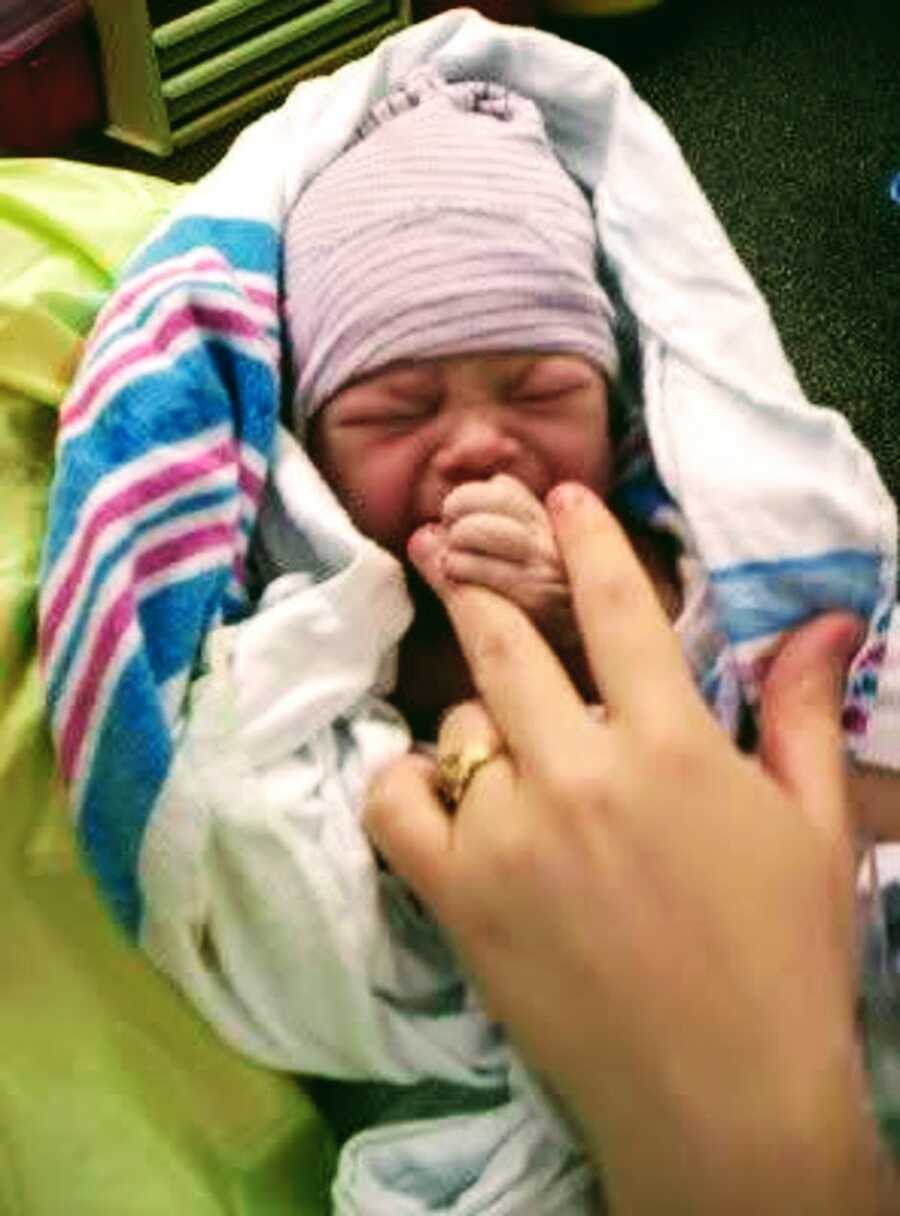 Baby girl grasps at her mother's finger.
