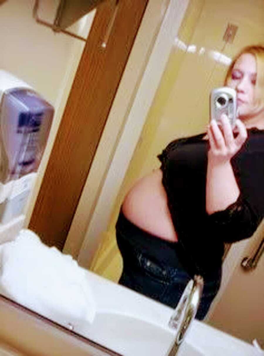 Teen girl taking mirror selfie with pregnant belly