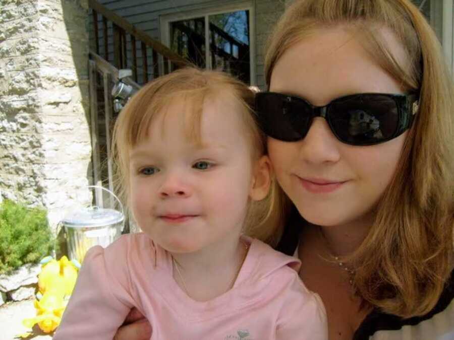 Teen mom wearing sunglasses embraces toddler