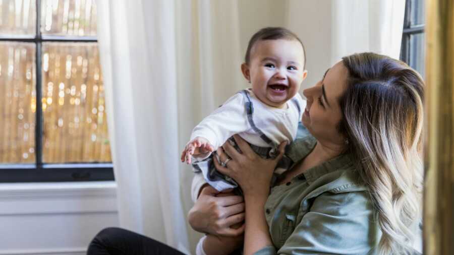 Mom holds laughing baby girl in her arms. 