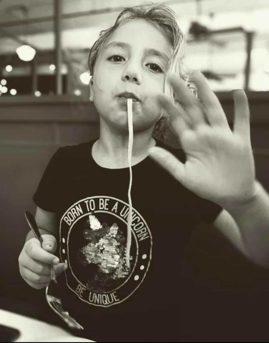 little girl using her hands to eat while a noodle hangs out of her mouth