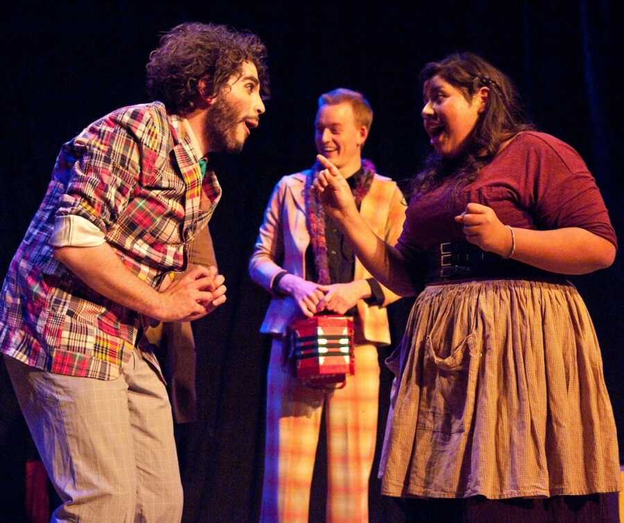 woman in maroon shirt and plaid apron on stage acting