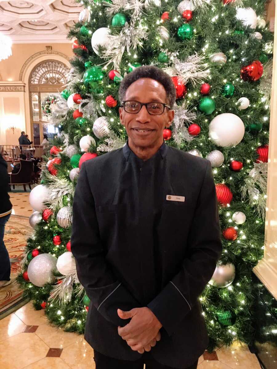 Hardworking bellhop smiling in front of a big Christmas tree at the lobby of the Omni Hotel 