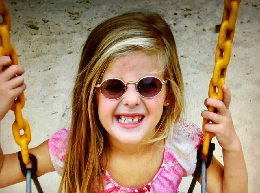 little girl with sunglasses on smiling on the swing
