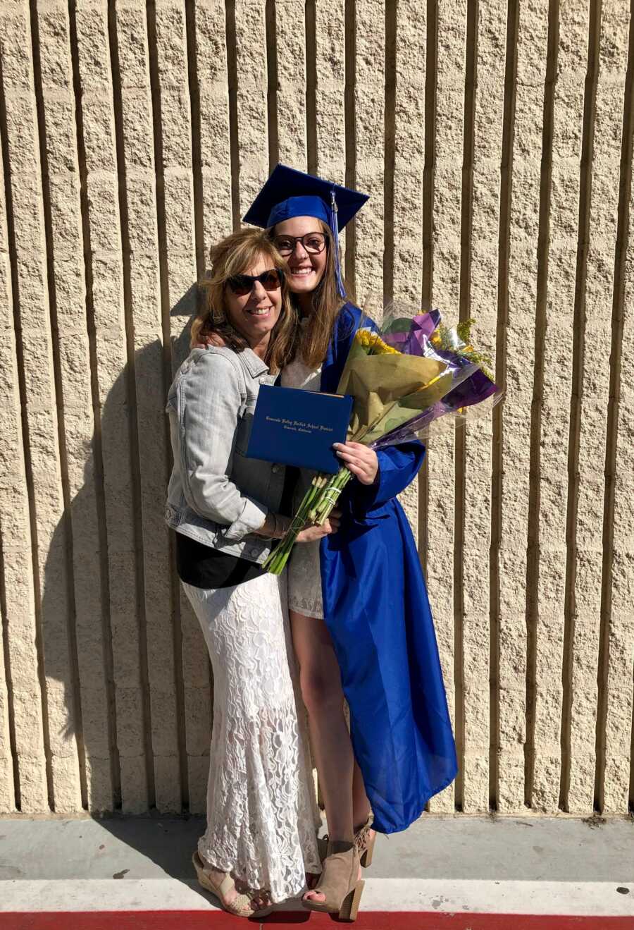 woman at graduation smiling and posing against a wall with her family member 
