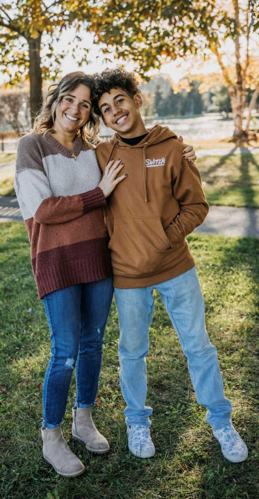 Mom and teenage son hugging and smiling outdoors wearing earthy colored clothing