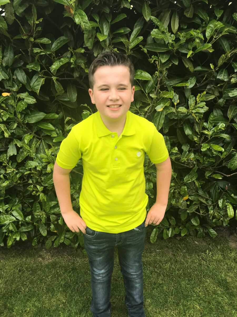 autistic boy posing in front of a bush in a bright lime shirt