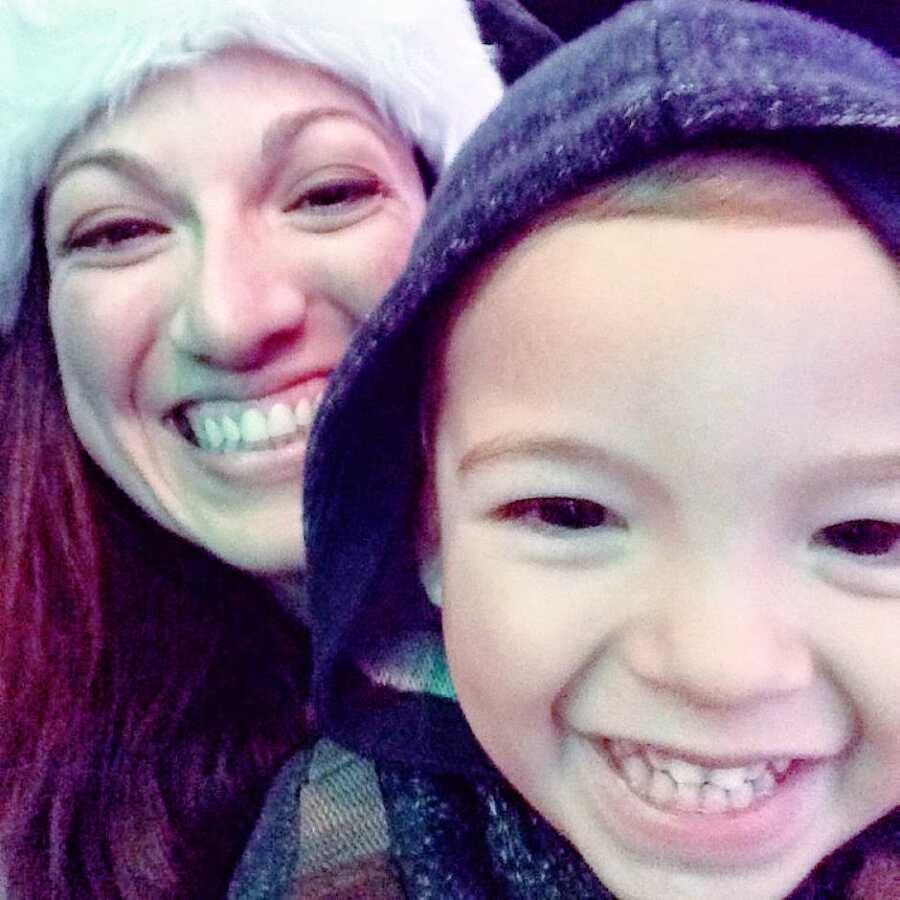 Mom and son take a selfie at a Christmas parade while the mom wears a Christmas Santa hat