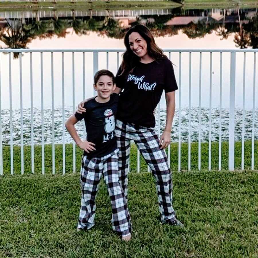 Mom and son pose for a photo in front of a lake with matching Christmas-themed pajamas on