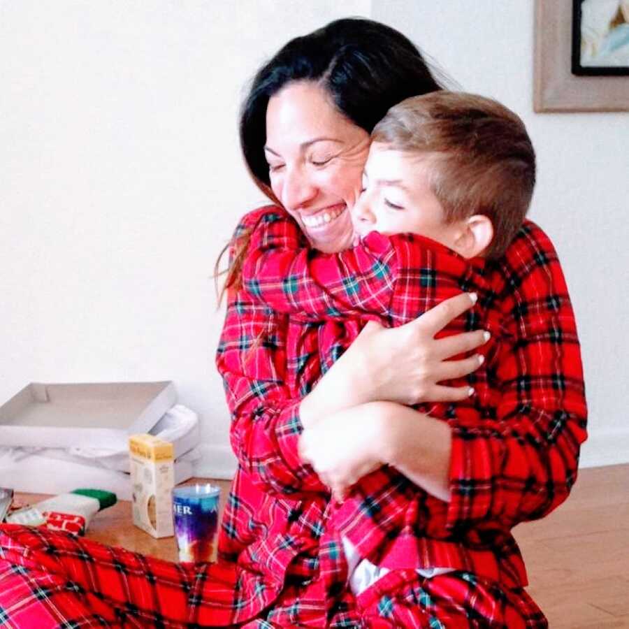 Mom and son embrace tightly while wearing matching red and black plaid pajamas