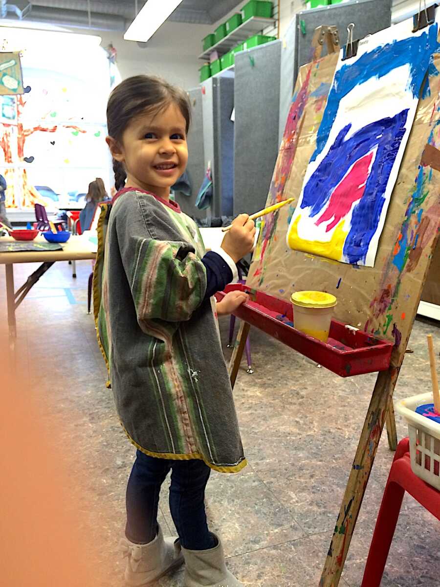 Young girl smiling while painting on a canvas in an art class