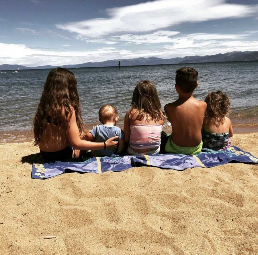 Sibling sitting on a towel at the beach contemplating the ocean 