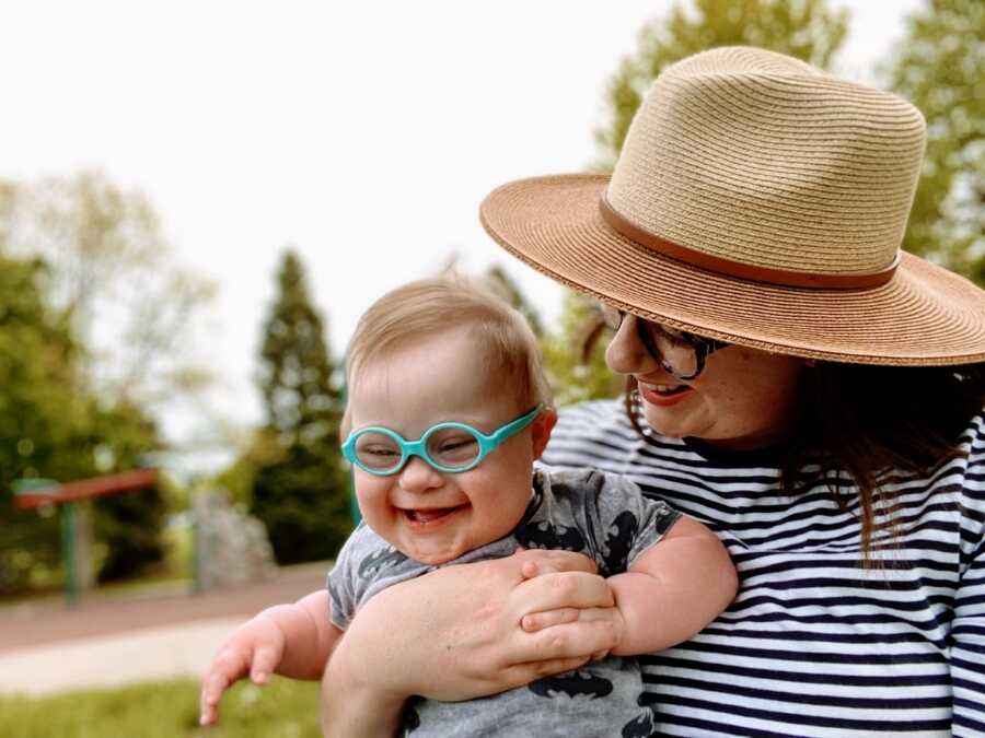Mom holds her son with Down syndrome outside while he laughs