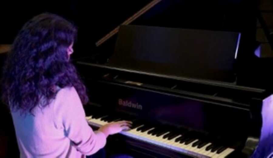 Woman plays the piano during recital with purple mood lighting