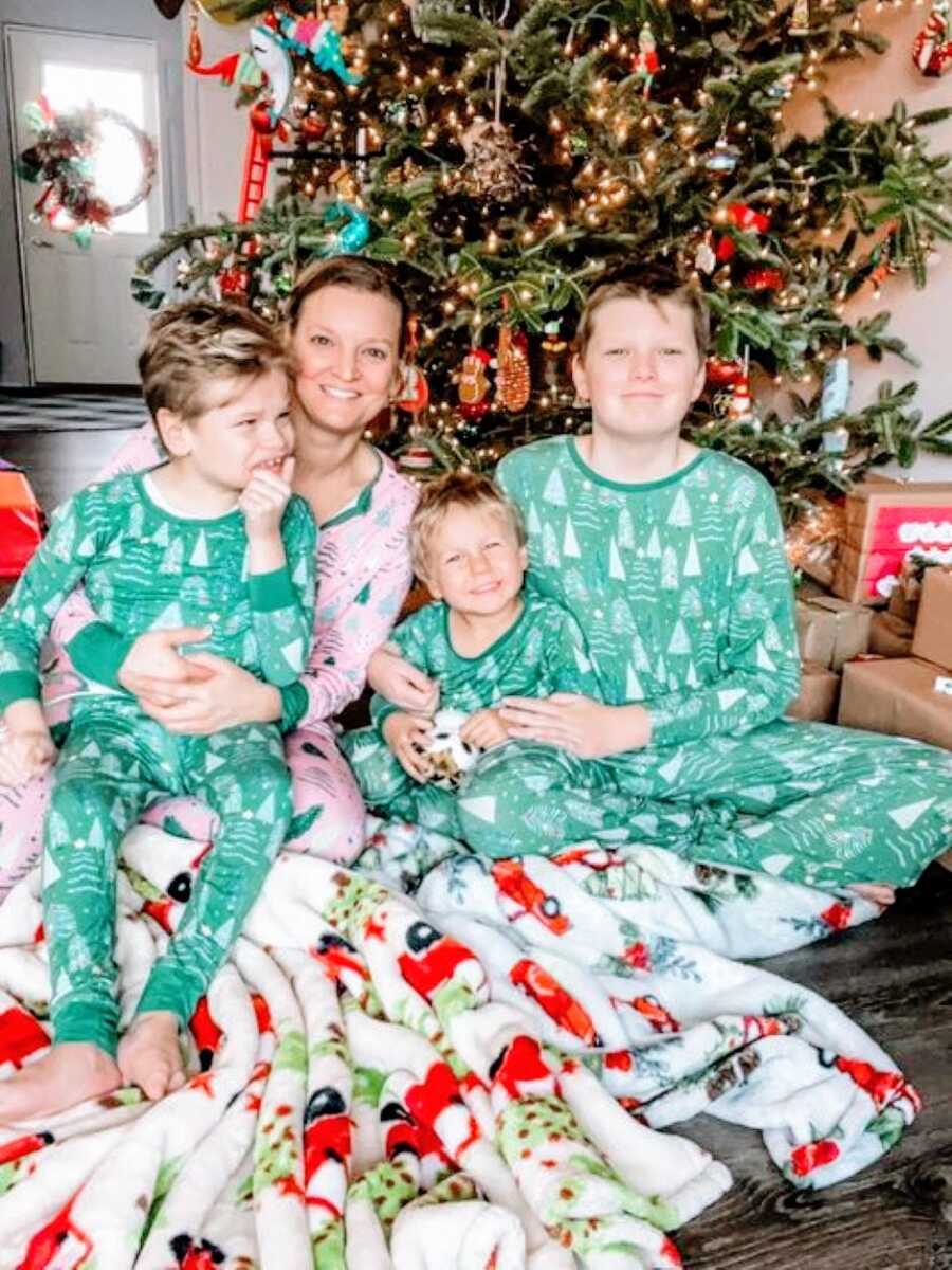 Mom takes a family photo with her three sons in front of the Christmas tree in matching pajamas