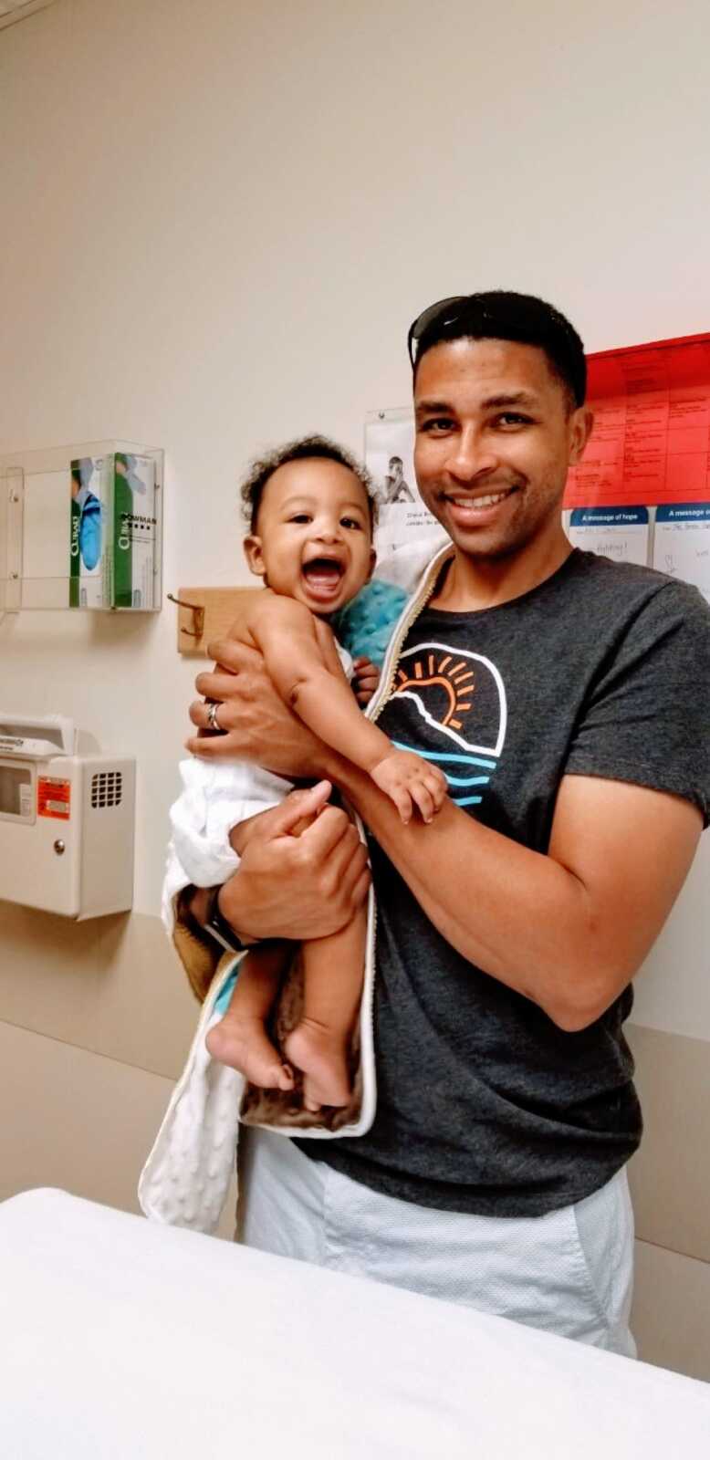 Little boy battling cancer smiles and laughs at the doctor's office while his dad holds him