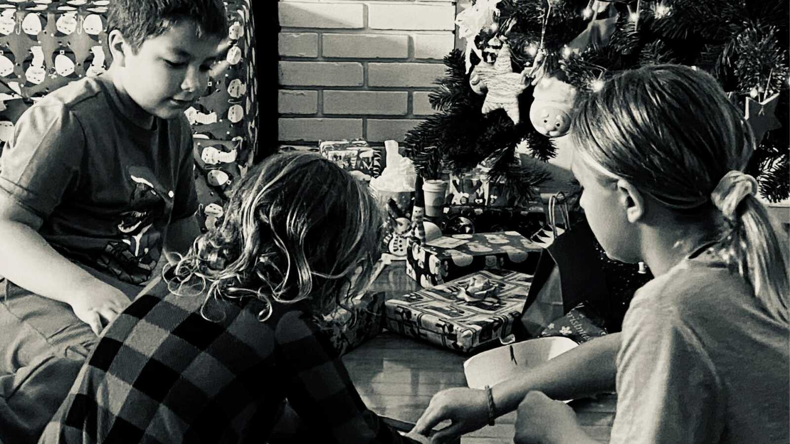 three kids opening up their presents by the tree
