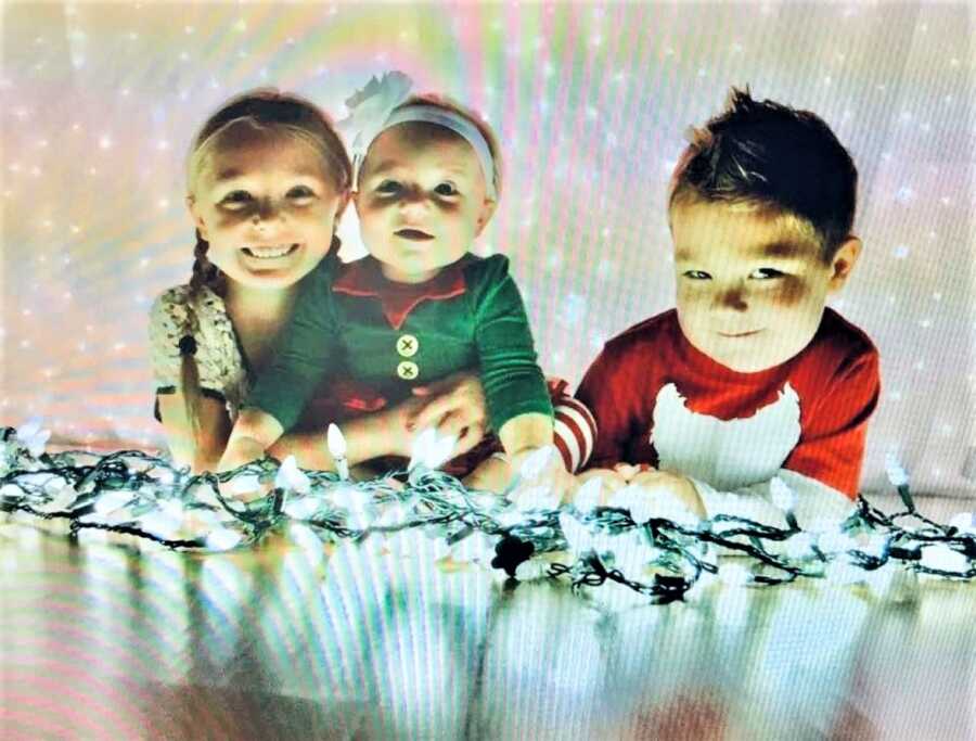three little kids posing by christmas lights for a photo