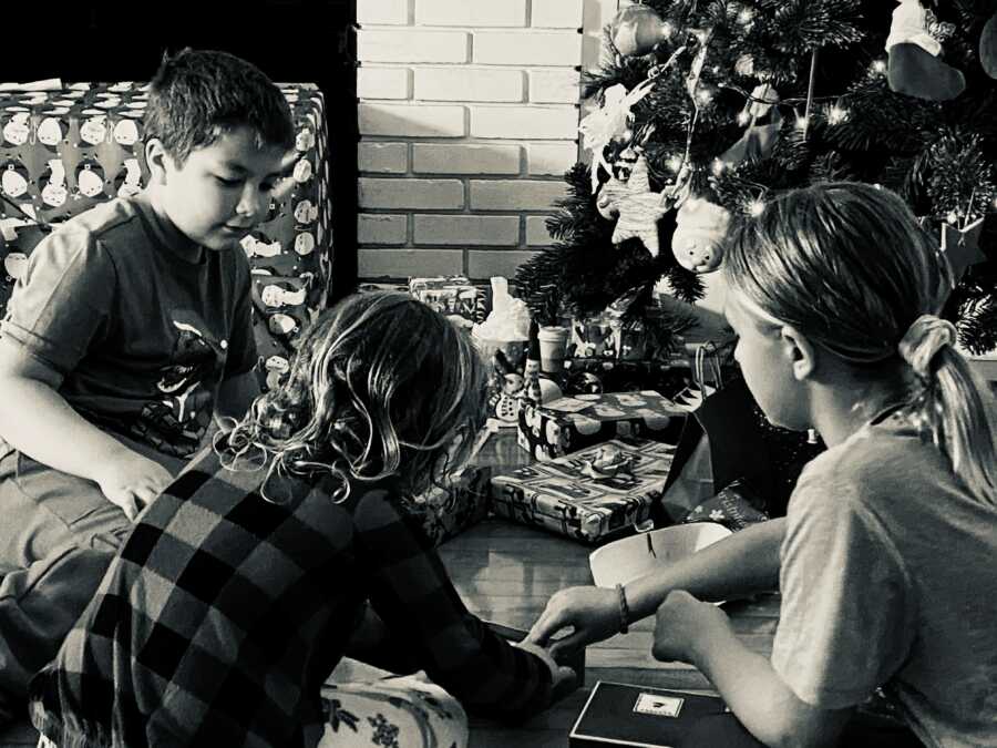 three kids opening up their presents by the tree