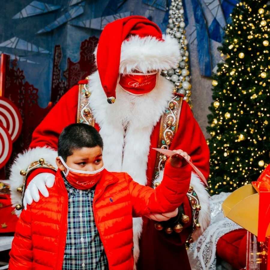 little boy and santa walking around the christmas trees