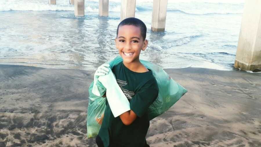 little boy picking up trash on the beach to help keep them clean