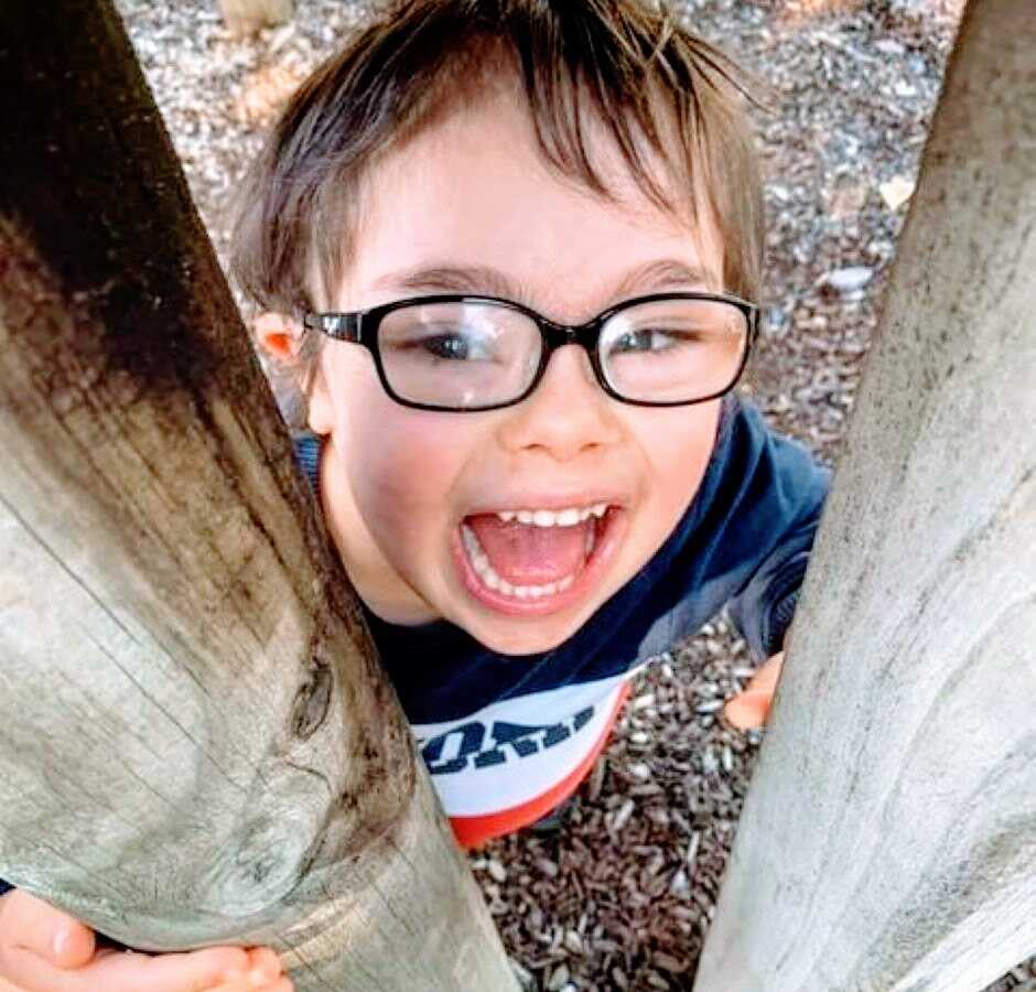 Special needs mom takes a photo of her son with down syndrome smiling and playing at the park