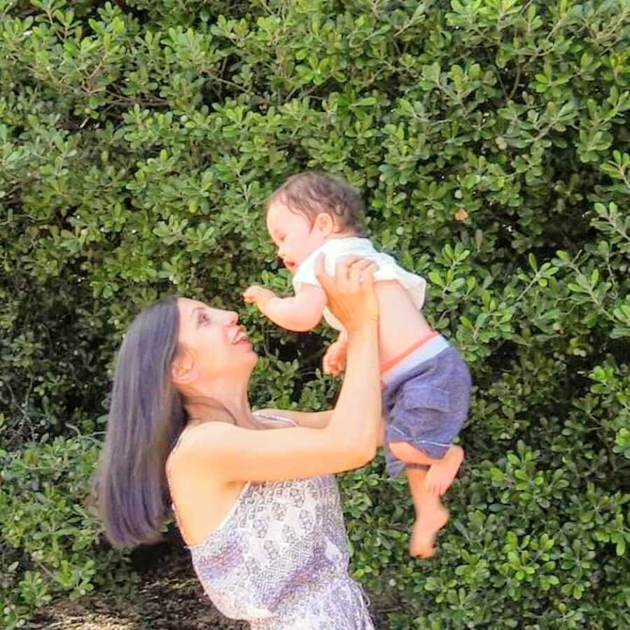 Special needs mom lifts her son with down syndrome up into the air while smiling at him