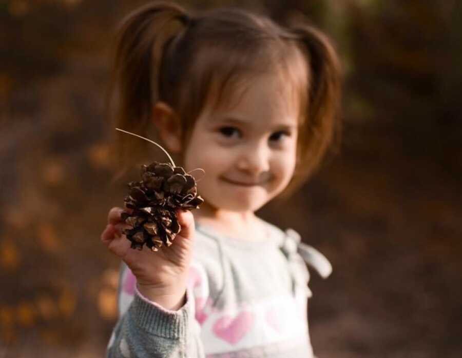 young girl holding a pine cone