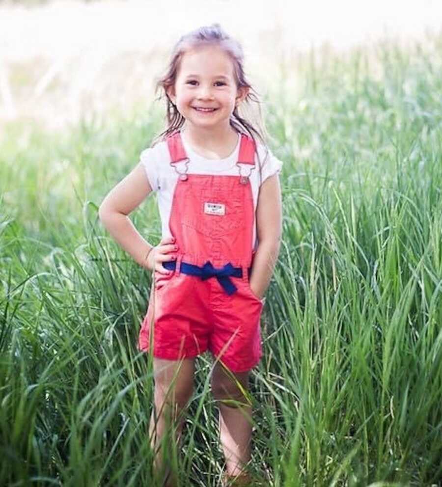 little girl in red overalls outside