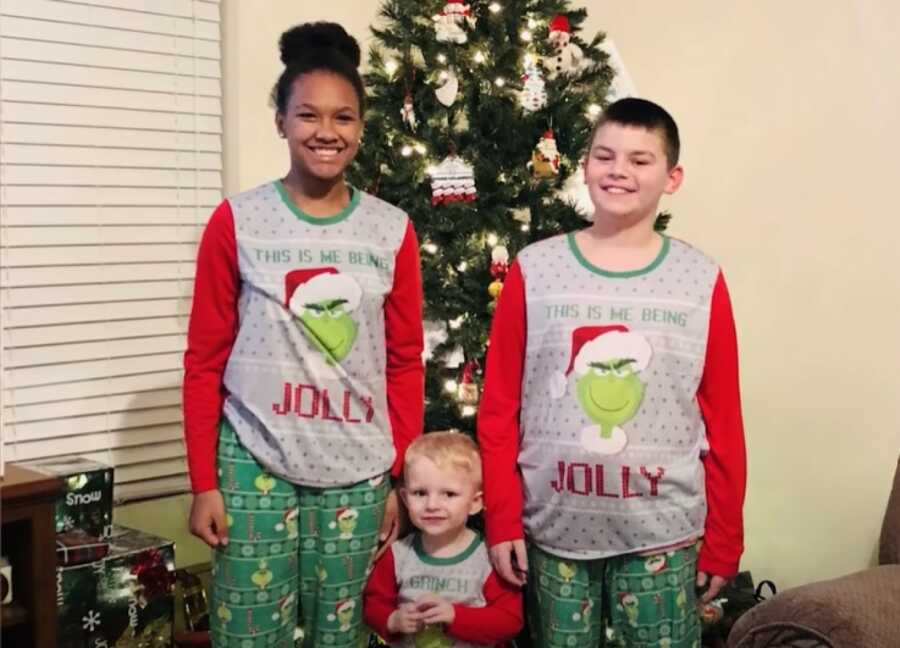 three kids in matching pjs in front of the tree