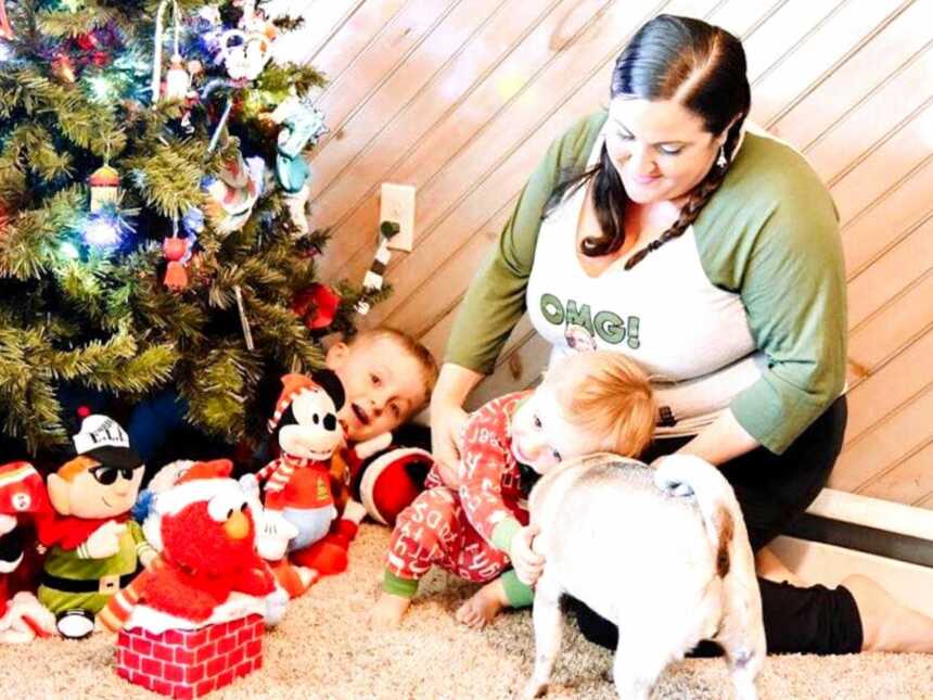 A mom sits near a Christmas tree with kids and dog
