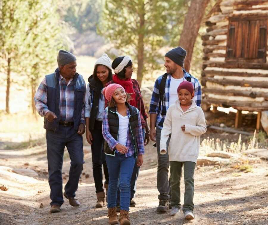 Family takes a walk outside their cabin, wearing flannels and jackets.