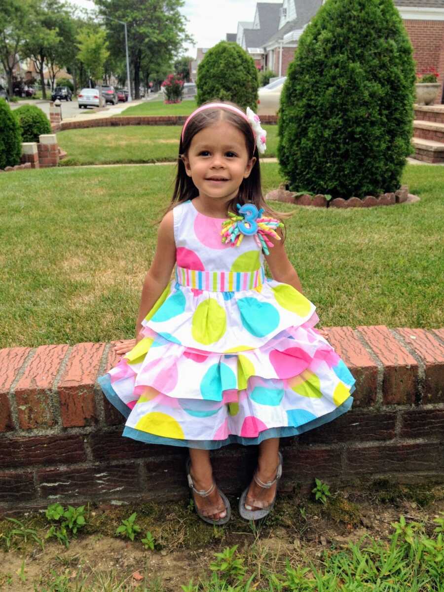 young girl posing on her third birthday in a colorful polkadot dress