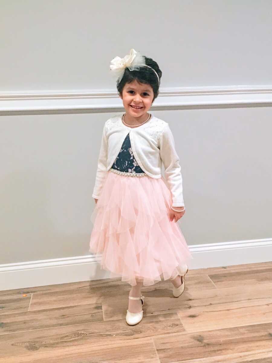 young girl poses with a dress on and a bow in her hair