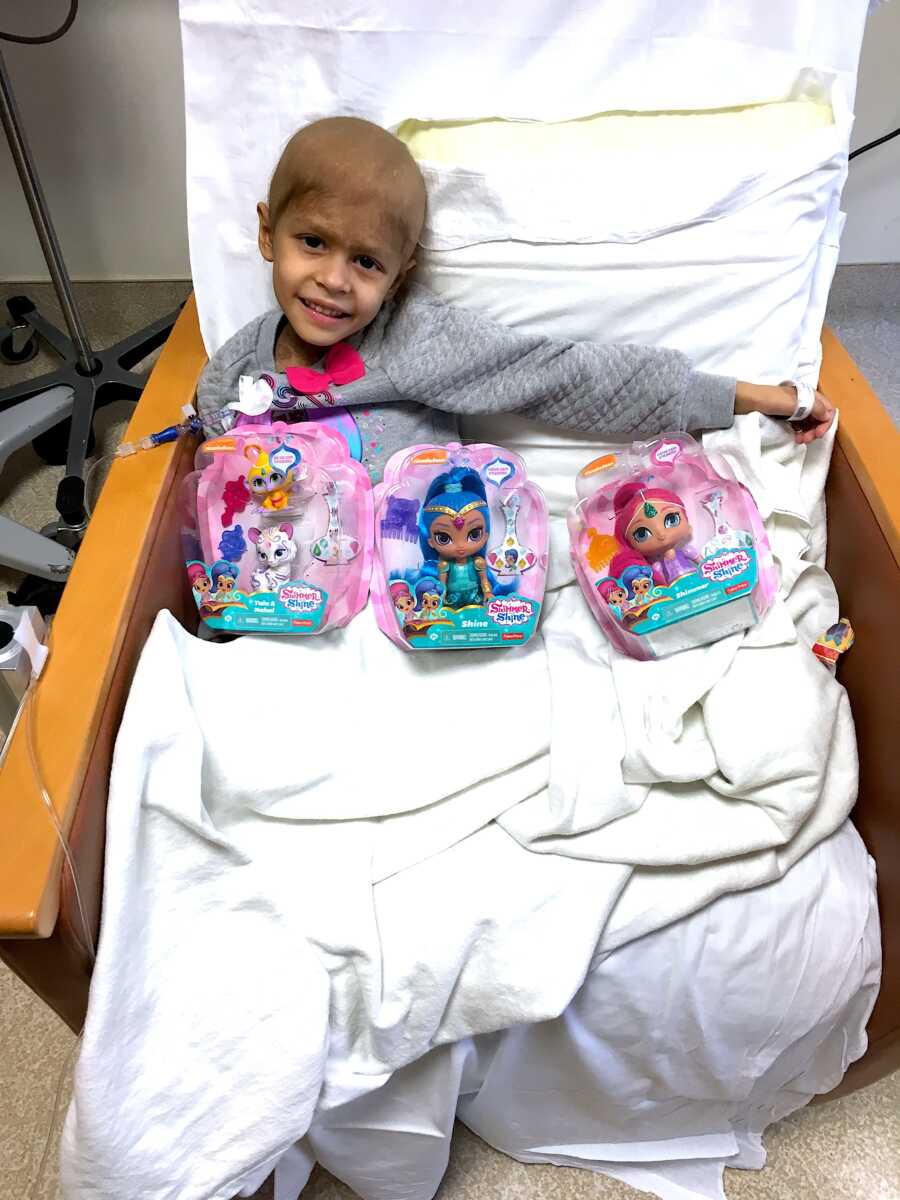 young girl with cancer in hospital sitting in chair with toys on her lap