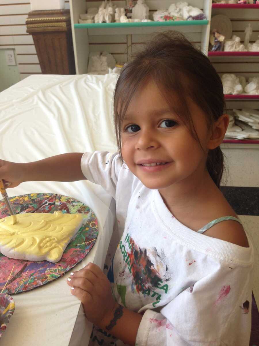 smiling young girl sitting at a table painting pottery