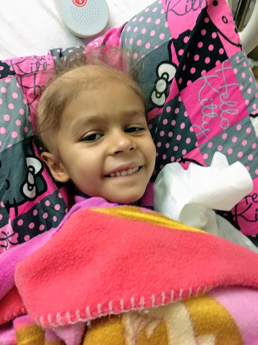 young girl with childhood cancer laying in hospital bed wrapped in blankets