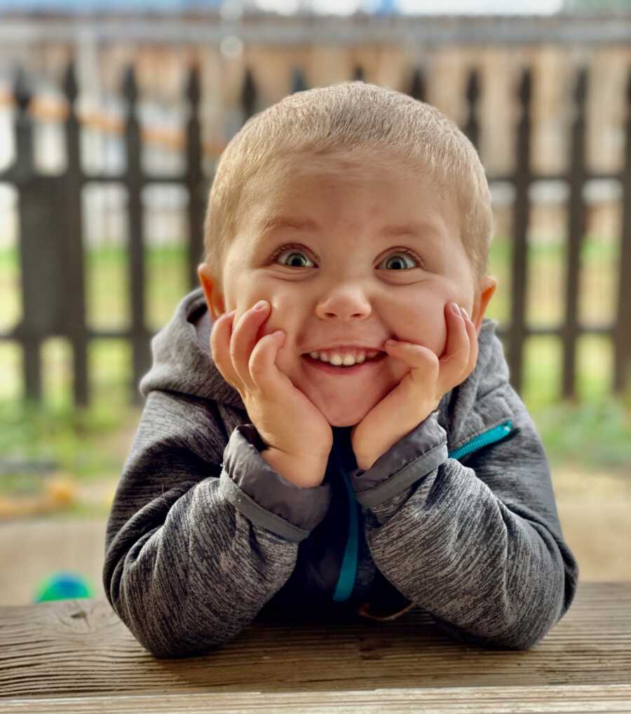 boy with his head in his hands making a face at the camera