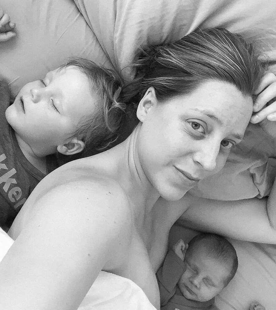 Freshly postpartum mom lays in bed with her babies. 