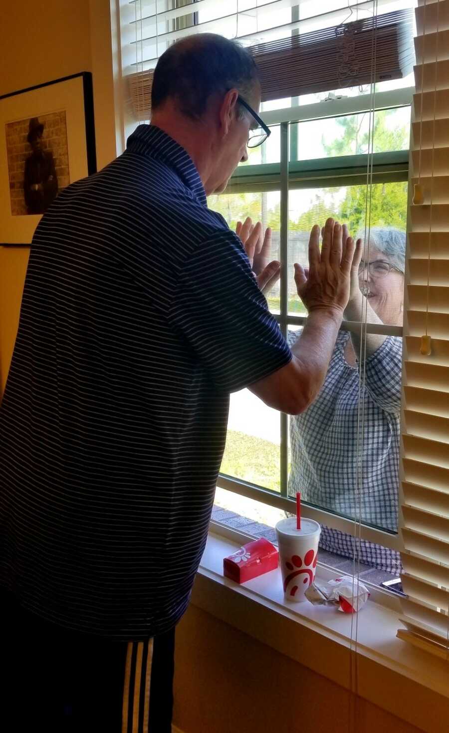 wife seeing her husband in a memory care home through a window