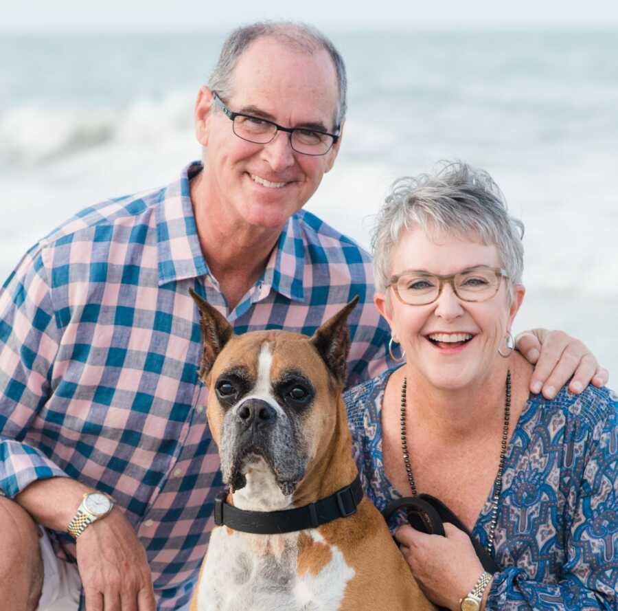 husband and wife posing together on a beach with their dog