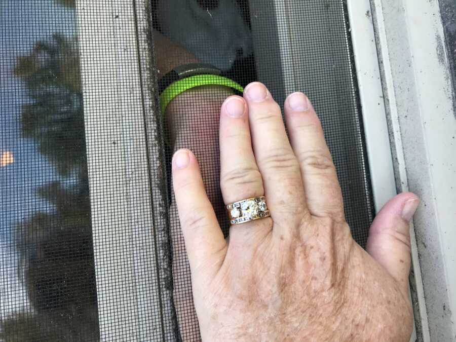 wife trying to hold husband's hand through window