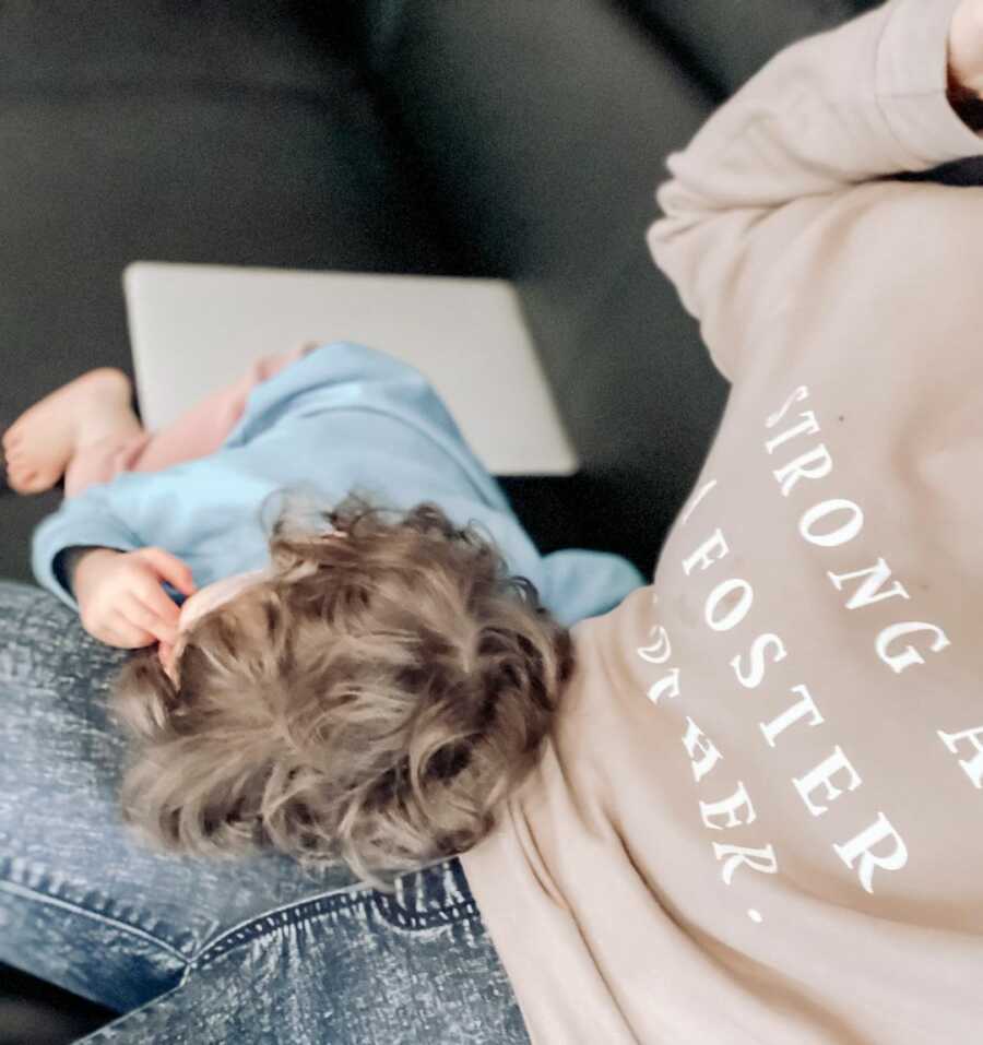 Foster mom sits on the couch while child rests their head in her lap.