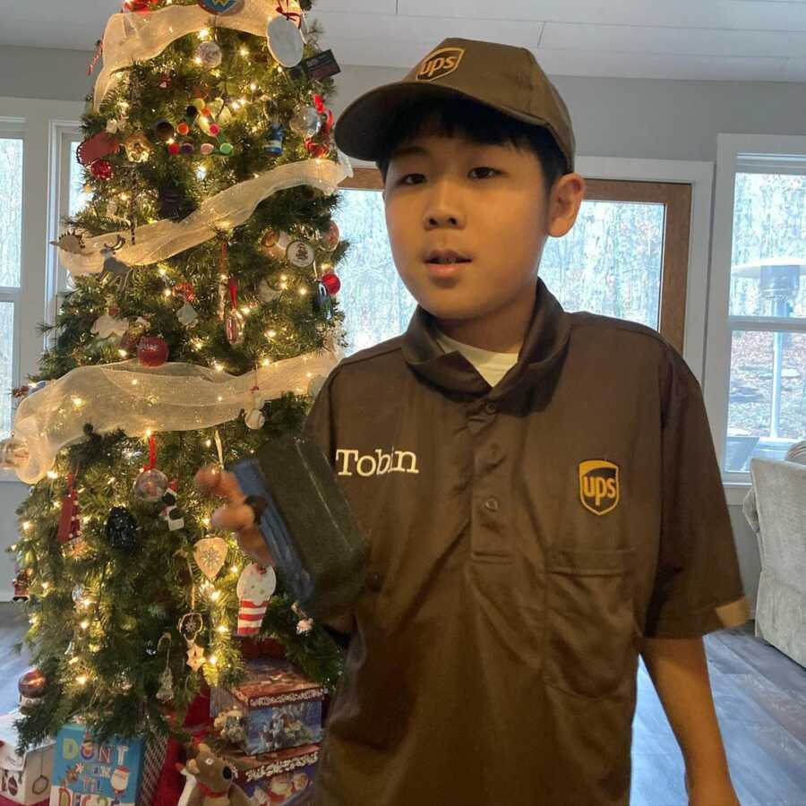 little boy posing in front of the christmas tree in his UPS uniform