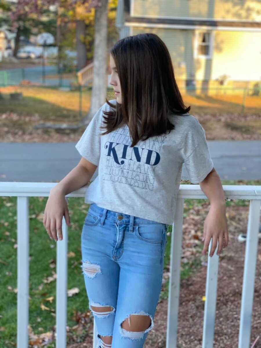  young girl in a kind shirt leaning against the railing for a picture