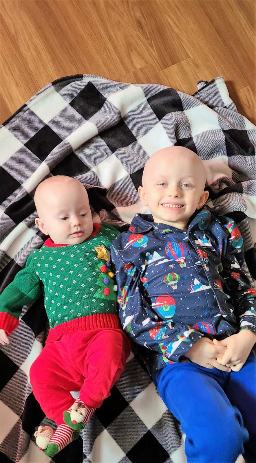5-year-old cancer survivor laying on the floor on top of a blanket with his baby brother wearing Christmas and Hot air balloon outfits 