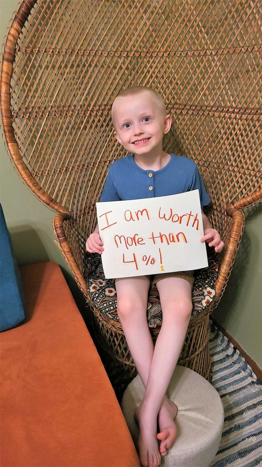 5-year-old caner survivor holding a sign that says 'I am worth more than 4%' referring to the 4% of funds that go to childhood cancer research